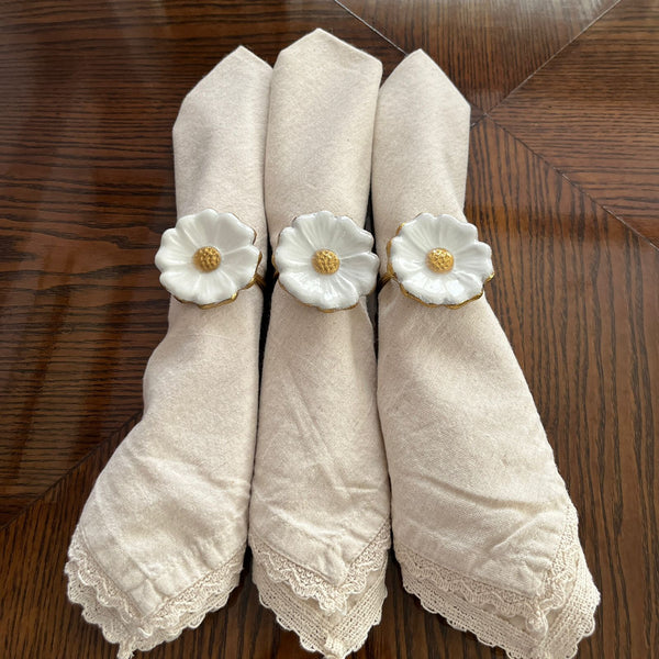 Set of six elegant napkin rings with white flower designs on beige napkins displayed on a wooden table.