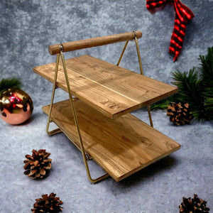 Anánta Acacia Wood 2-Tier Platter displayed on a festive background with pine cones and a holiday ribbon, showcasing its elegant wood grain and portable design.