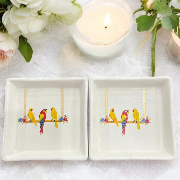 Chatterbox Trinket Platter – A charming set of 4x4-inch stoneware plates featuring vibrant birds on a floral swing, accented with 24-carat gold, perfect for small treasures.