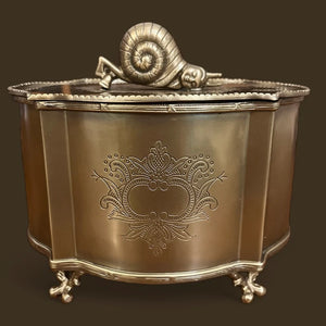 Close-up of a Zen Brass Storage Box with ornate floral engravings and a snail-shaped handle on the lid, set against a dark background. The brass box rests on delicately crafted feet, emphasizing its luxurious and detailed craftsmanship.