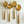 An elegant set of four Amála serving spoons with a shiny gold finish, featuring distinct designs: a deep ladle, a flat spoon, a solid spoon, and a unique spaghetti/noodle spoon, all with ornate twisted handles displayed on a marble surface.