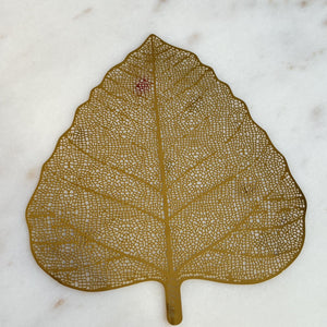 A delicate Stainless Steel Bookmark shaped like a "bodhi" leaf with intricate laser-cut patterns, showcasing its artistic design. This elegant piece also serves as a versatile mug cover, blending style with functionality.